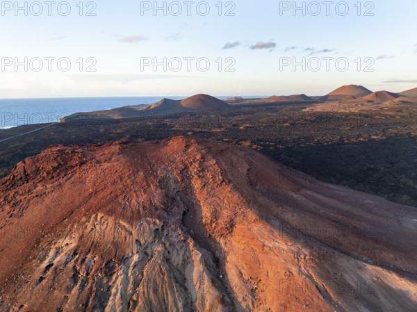 Picturesque volcanic landscape in evening light, red volcano Montaña Bermeja between lava fields, aerial view, Lanzarote, Canary Islands, Spain