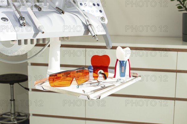 On the tray are various dental instruments, a model dental implant and bright orange safety glasses, ready for use in clinical dental settings