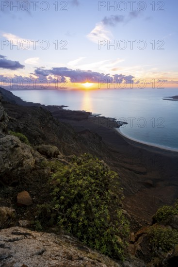 View from steep cliffs to sea and coast with sun stars, Mirador del Porrito viewpoint at sunset, Lanzarote, Canary Islands, Spain