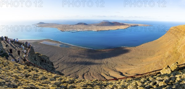 View of La Graciosa island with volcanic craters in the evening light, tourists on an observation deck at the Mirador del Río viewpoint designed by artist César Manrique, Lanzarote, Canary Islands, Spain