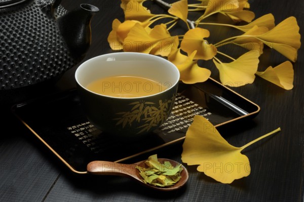 Ginkgo tea in tea bowl and ginkgo leaf, tea leaves in a spoon, ginkgo biloba