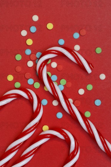 Candy canes and sugar confetti against red background, Christmas