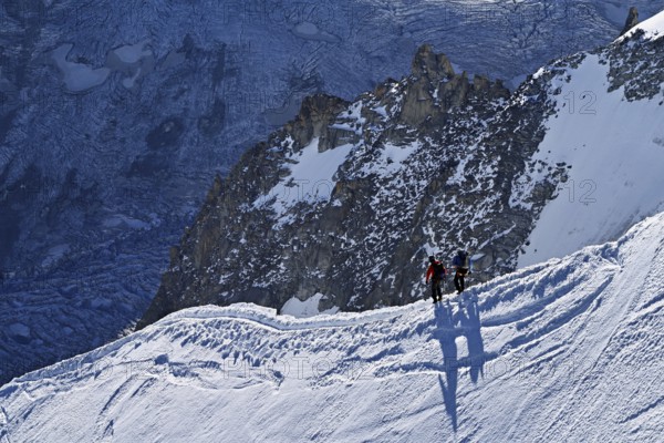 Two ascended mountaineers run across a snow-covered mountain ridge, Aiguille du Midi, Chamonix-Mont-Blanc, Haute-Savoie, France
