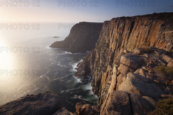 Long exposure shows sunset over the cliffs of Cape Raoul. Golden light hits the sea and colors the rocks warmly in the evening. Cape Raoul, Tasman Peninsula, Tasmania, Australia