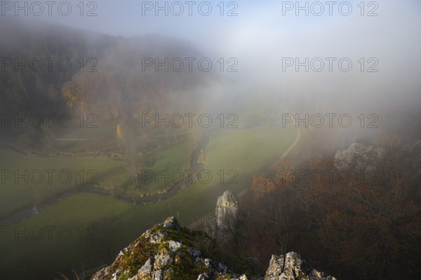 Autumn landscape with rising fog over the Grosse Lauter river loop in Lautertal at sunrise. View from above of the picturesque valley with colorful deciduous forest and rolling hills, Großes Lautertal, Baden-Württemberg, Germany