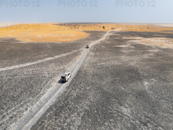 Aerial view, two off-road cars driving on a salt pan, arid landscape, Botswana
