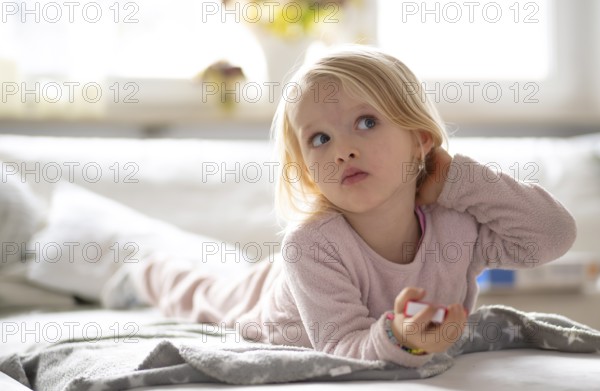 Child, girl, 4 years, blonde, lying on sofa, watching TV, watching television, watching television, excited, Stuttgart, Baden-Württemberg, Germany