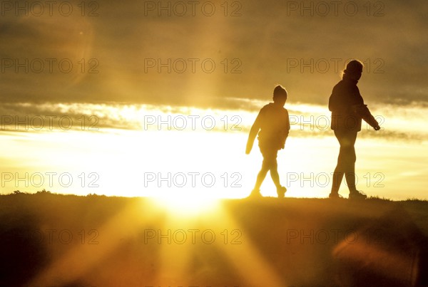 Woman and child walk across a dike on the island of Fehmarn at sunset, 13.10.2025, Fehmarn, Schleswig-Holstein, Germany