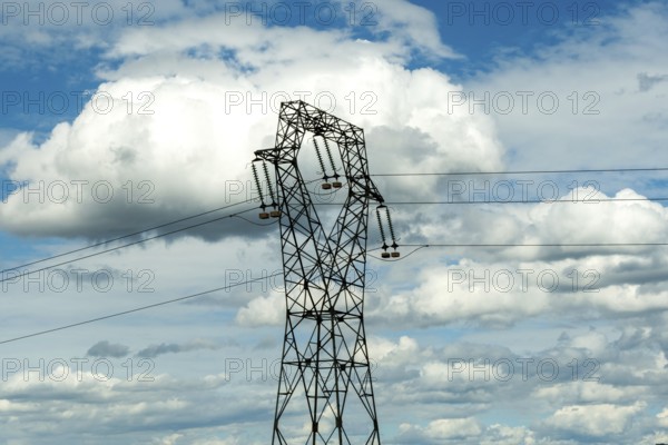 High voltage power lines against a bright blue sky with scattered clouds, Puy de Dome, Auvergne Rhone Alpes, France