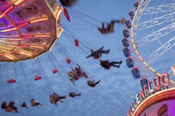An illuminated chain carousel turns at night at a funfair, with floating people and colourful lights, Bad Cannstatt, Stuttgart, Baden-Württemberg, Germany