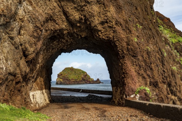 View of the small island of Ilhéu da Ribeira da Janela, Madeira, Portugal, through a tunnel carved into the rock on the old ER 101 coastal road