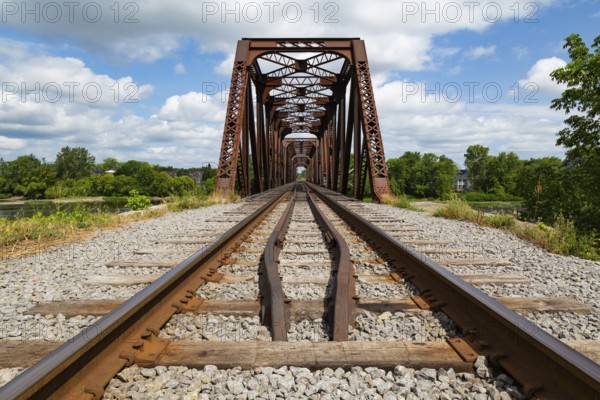 Railroad tracks leading to old rusted Terrebonne Pratt truss railroad bridge over Des Mille-Iles river in summer, Laval, Quebec, Canada