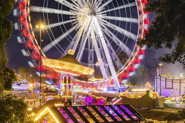 Folk festival in Stuttgart. The 178th Cannstatter Volksfest on the Wasen is one of the most important traditional festivals in Germany. Ferris wheel, chain carousel and other amusement park attractions, light effects at night. Stuttgart, Baden-Württemberg, Germany