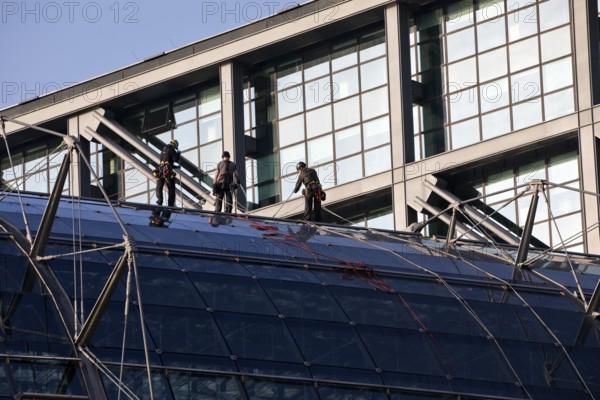 Three male glass cleaners abseiling down a glass roof of Berlin Central Station to clean windows, Berlin, Germany