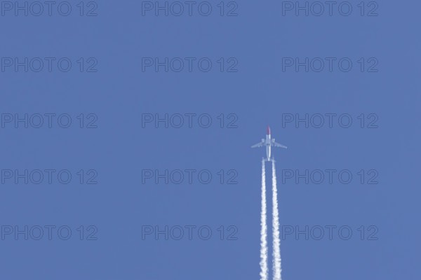 Boeing 737 jet passenger aircraft of Norweign Air with a vapour trial or contrail behind flying in a blue sky, England, United Kingdom