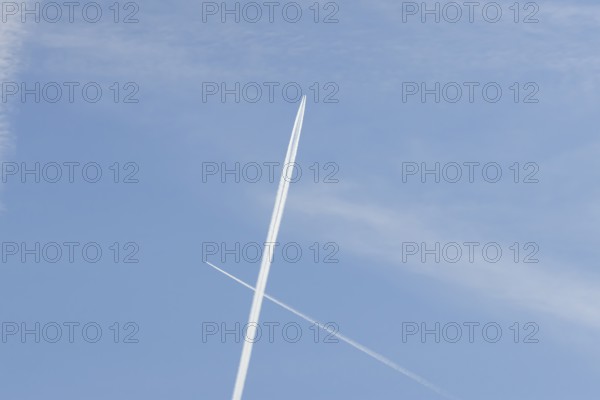 Two jet passenger aircraft with vapour trails or contrails flying in a blue sky crossing making a cross, England, United Kingdom