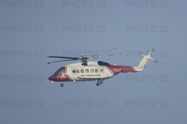 Sikorsky S-92A helicopter of the UK HM Coastguard flying in a blue sky, England, United Kingdom