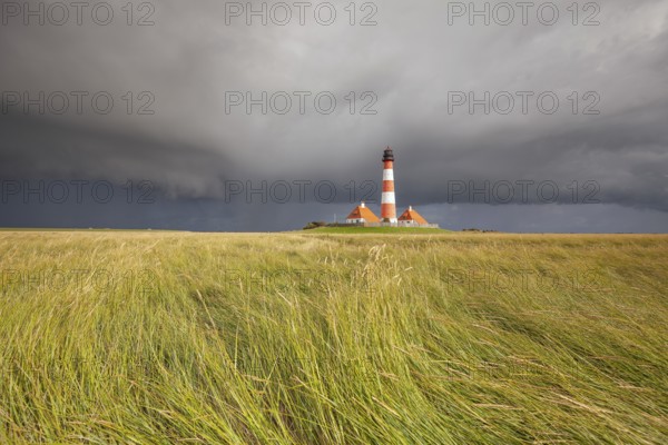 Illuminated Westerheversand lighthouse on the North Sea under dark storm clouds