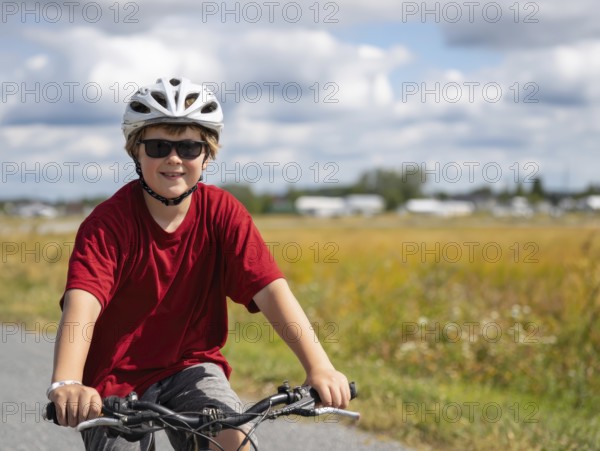 A boy with a bicycle helmet rides a bicycle and smiles friendly into the camera, AI generated, AI generated