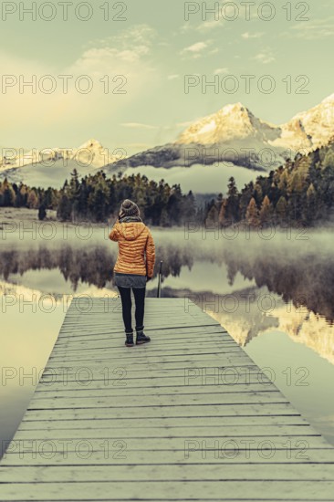 Young woman at Lake Staz near Sankt Moritz in the Engadine in Switzerland. Morning atmosphere with fog in autumn. Reflection of water