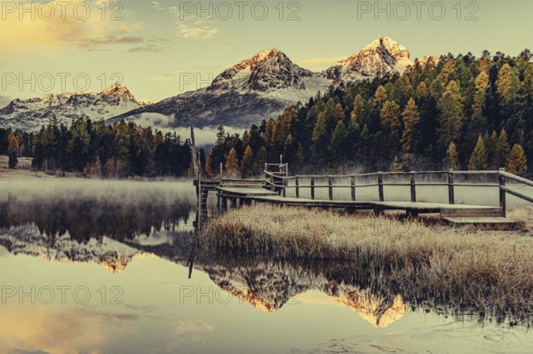 Lake Staz near Sankt Moritz in the Engadin in Switzerland. Morning atmosphere with fog in autumn. Water reflection and snow-covered mountains in the background