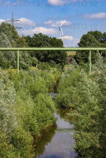 Bottrop, North Rhine-Westphalia, Germany - Renaturalised Boye, the tributary of the Emscher, has been transformed into a near-natural watercourse, flood protection through newly designed flooding areas, the Boye is now free of wastewater following the construction of a parallel sewer, is part of the Emscher river system and thus part of the Emscher conversion, was previously an open, above-ground wastewater channel, mixed water channel with surface water and wastewater. Wind turbine on the Mottbruch spoil tip at the back