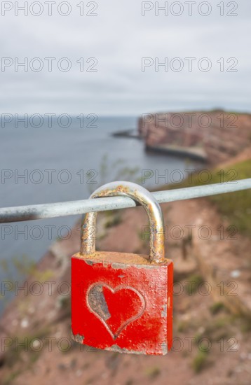 Red padlock with engraved heart symbol on a wire rope in front of the steep coast, red cliff of Heligoland, in the background the Lange Anna, view of the sea, love lock, rusty and romantic, Heligoland, Schleswig-Holstein, North Sea, Germany