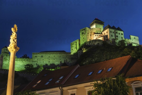Night shot of the plague column column commemorating the victims of the plague at the beginning of the 18th century, in the background is Trencín Castle, Capital of Culture 2026, Trencín, Slovakia