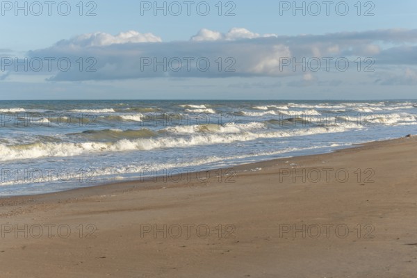 The waves crash gently against a rocky shoreline at sunset, creating a tranquil atmosphere. The sandy beach is strewn with pebbles and surrounded by a beautiful sky. Plage de l'Aubraie, Les Sables d'Olonne, Vendee, France