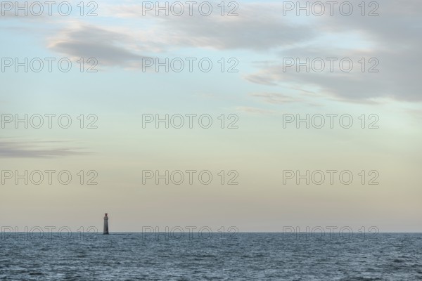 A lighthouse rises from the gentle waves of the ocean, surrounded by a tranquil seascape. Soft clouds drift over the sunset, creating a peaceful atmosphere. Les Sables d'Olonne, Vendee, France