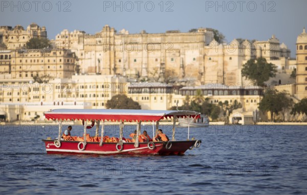 Excursion boat on Lake Pichola, behind the City Palace in the evening light, Udaipur, Rajasthan, India