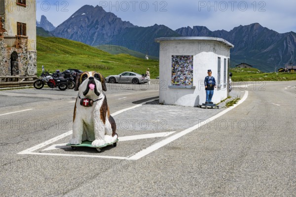 Disused former border hut for passport control at the border crossing between France and Italy, in the foreground figure of a St Bernard dog with a barrel around its neck, behind it figure of a French border official, Graian Alps, Département Savoie, France, Valle d'Aosta, Italy