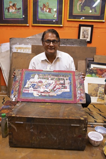 Miniature painter, 50 years old, shows a picture of the royal city palace in his studio, Udaipur, Rajasthan, India
