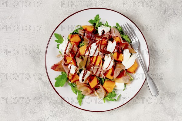 Salad with slices of ripe melon, prosciutto, mozzarella and fresh arugula, decorated with balsamic glaze