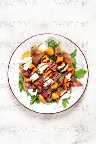 Salad with slices of ripe melon, prosciutto, mozzarella and fresh arugula, decorated with balsamic glaze