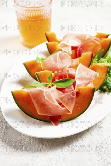 Cantaloupe melon with prosciutto and fresh basil, on a white plate, natural light