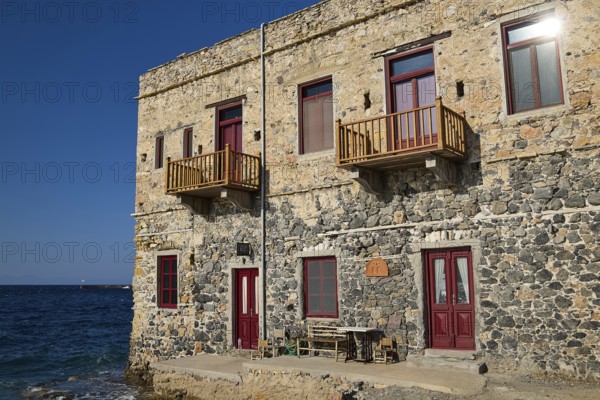 Stone house with red windows and balconies right on the waterfront in sunny weather, Agia Marina, Leros, Dodecanese, Greek Islands, Greece
