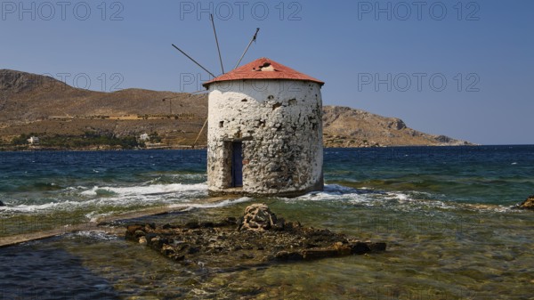 Historic windmill in the clear blue of the sea, surrounded by the rocky shore and bright sky, Agia Marina, Leros, Dodecanese, Greek Islands, Greece