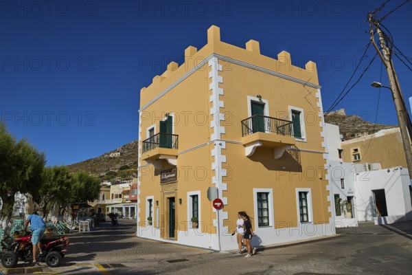 Mediterranean-style corner building with balconies and passers-by under a clear blue sky, Agia Marina, Leros, Dodecanese, Greek Islands, Greece
