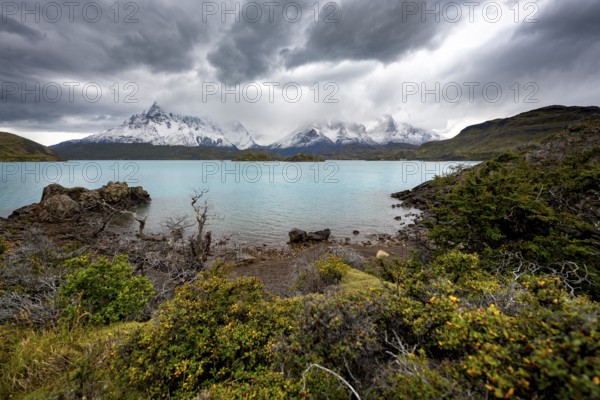 Cloudy mountain range Cuernos del Paine, shore of the blue lake Lago Pehoe in the evening light, dramatic sky, Torres del Paine National Park, Chile