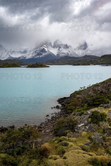 Cloudy mountain range Cuernos del Paine, shore of the blue lake Lago Pehoe in the evening light, dramatic sky, Torres del Paine National Park, Chile