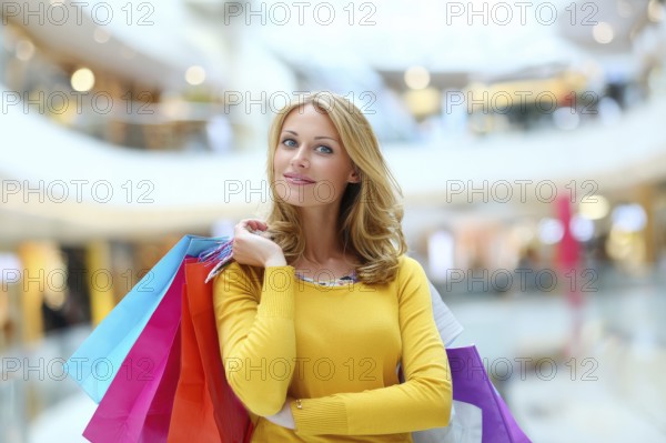 Beautiful young happy attractive woman with bags of different colours in shopping center mall shopping for brand name fashion items, AI generated