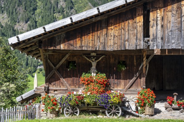 Colourful floral decorations and crucifix at a rustic alpine hut, Ridnauntal, South Tyrol, Italy
