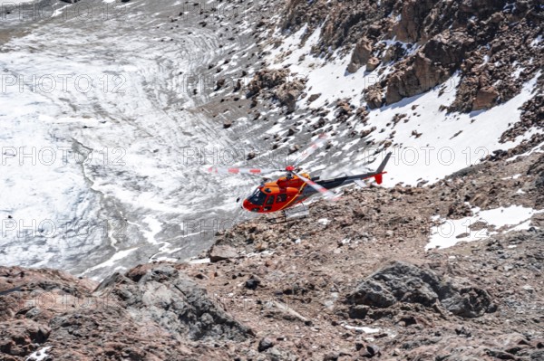 Red helicopter flies over glaciers in the mountains, Stubai Alps, South Tyrol, Italy
