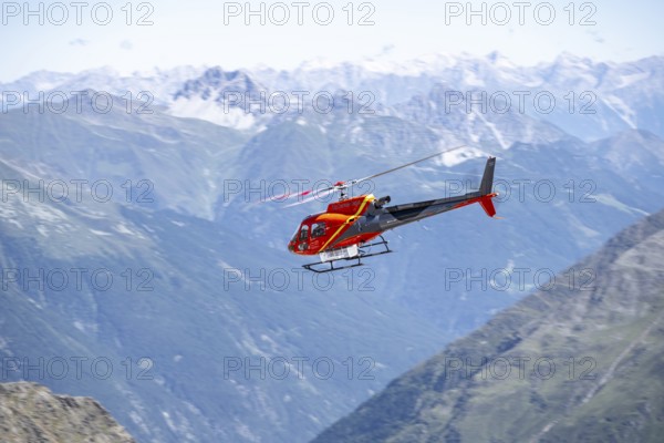 Red helicopter flying in the mountains, Stubai Alps, South Tyrol, Italy