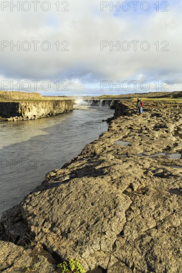 Hikers at the river Jökulsa a Fjöllum, canyon, waterfall Selfoss on the horizon, North Iceland, Iceland