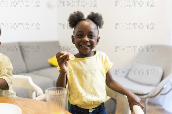 Smiling young girl savoring a delicious sweet treat while sitting at the dining room table, radiating joy and happiness in her home