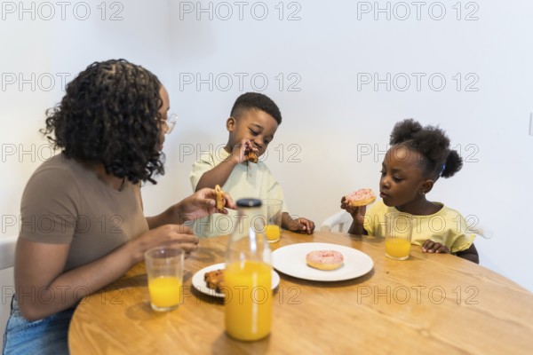 Mother and children enjoying breakfast together at home, sharing delicious donuts and refreshing orange juice around the kitchen table