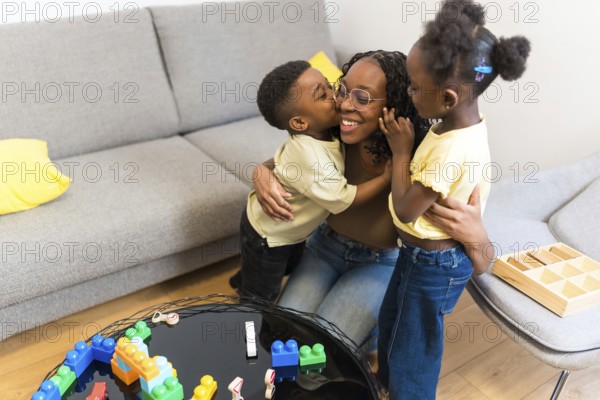 Cheerful mother enjoying time with her two loving children, embracing and kissing in the living room
