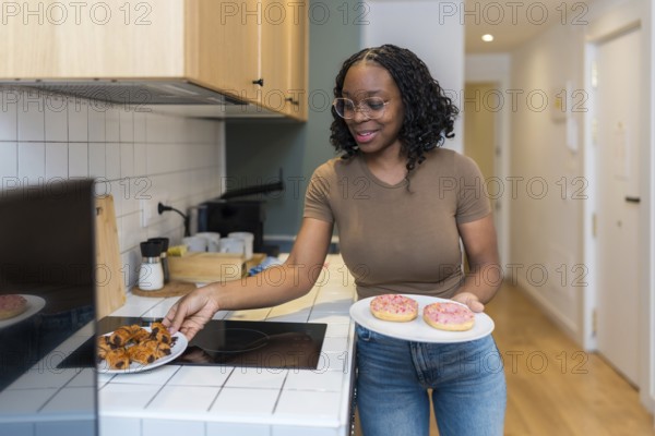 Young woman arranging donuts and pastries on plates in a modern kitchen, getting ready for a sweet breakfast